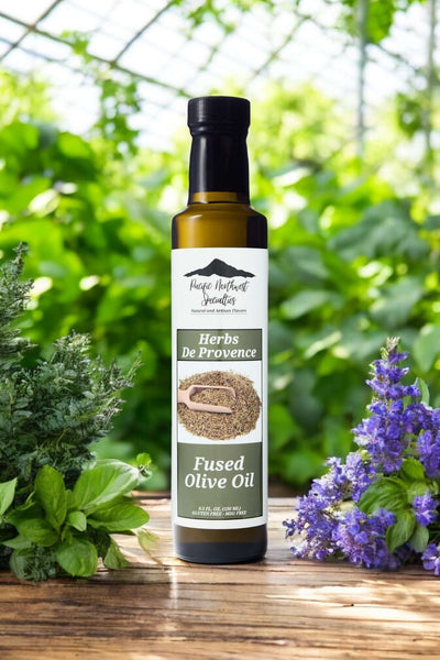 Herb De Provence Fused Olive Oil bottle surrounded by fresh herbs in a sunny garden setting. Perfect for enhancing dishes.