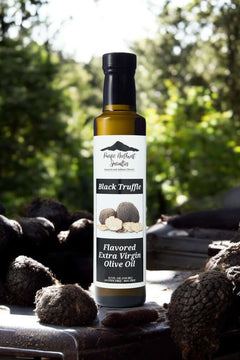 Black Truffle Flavored Extra Virgin Olive Oil bottle surrounded by truffles in a natural setting.