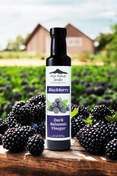 Bottle of Blackberry Dark Balsamic Vinegar surrounded by fresh blackberries on a farm.