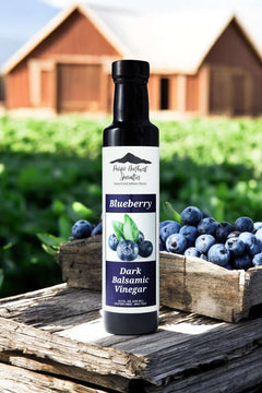 Blueberry Dark Balsamic Vinegar bottle in a rustic setting with fresh blueberries in wooden crate.