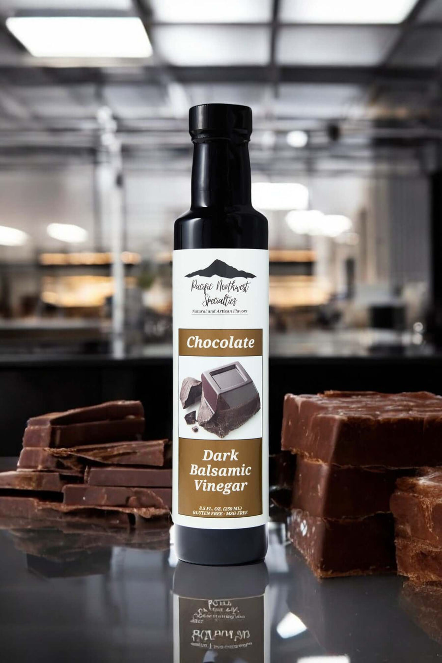 Bottle of Chocolate Dark Balsamic Vinegar with chocolate pieces in the foreground, perfect for desserts and marinades.