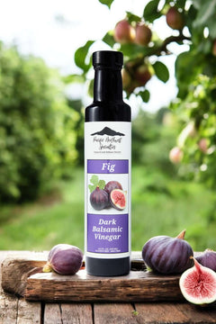 Fig Dark Balsamic Vinegar bottle surrounded by fresh figs in a natural setting.