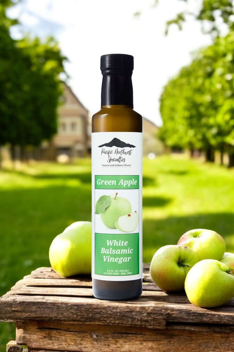Green Apple White Balsamic Vinegar bottle on a wooden crate with fresh green apples in an outdoor setting.