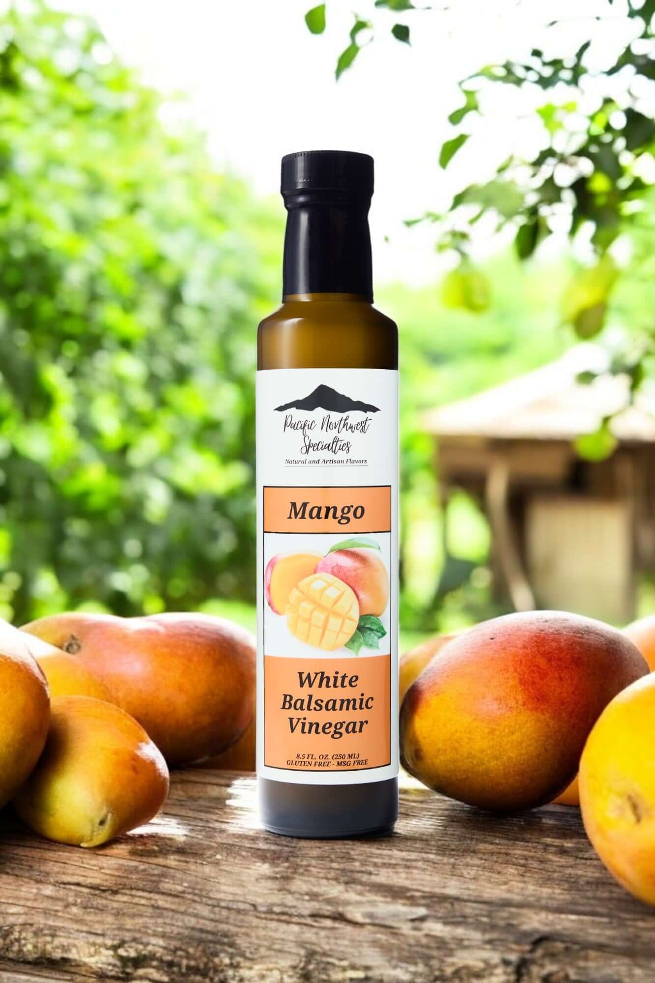 Bottle of Mango White Balsamic Vinegar surrounded by fresh mangos on a rustic table in a tropical setting.