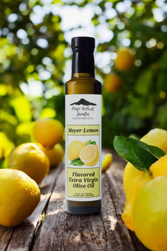 Meyer Lemon Extra Virgin Olive Oil bottle surrounded by fresh lemons on a wooden table, showcasing vibrant citrus flavor.