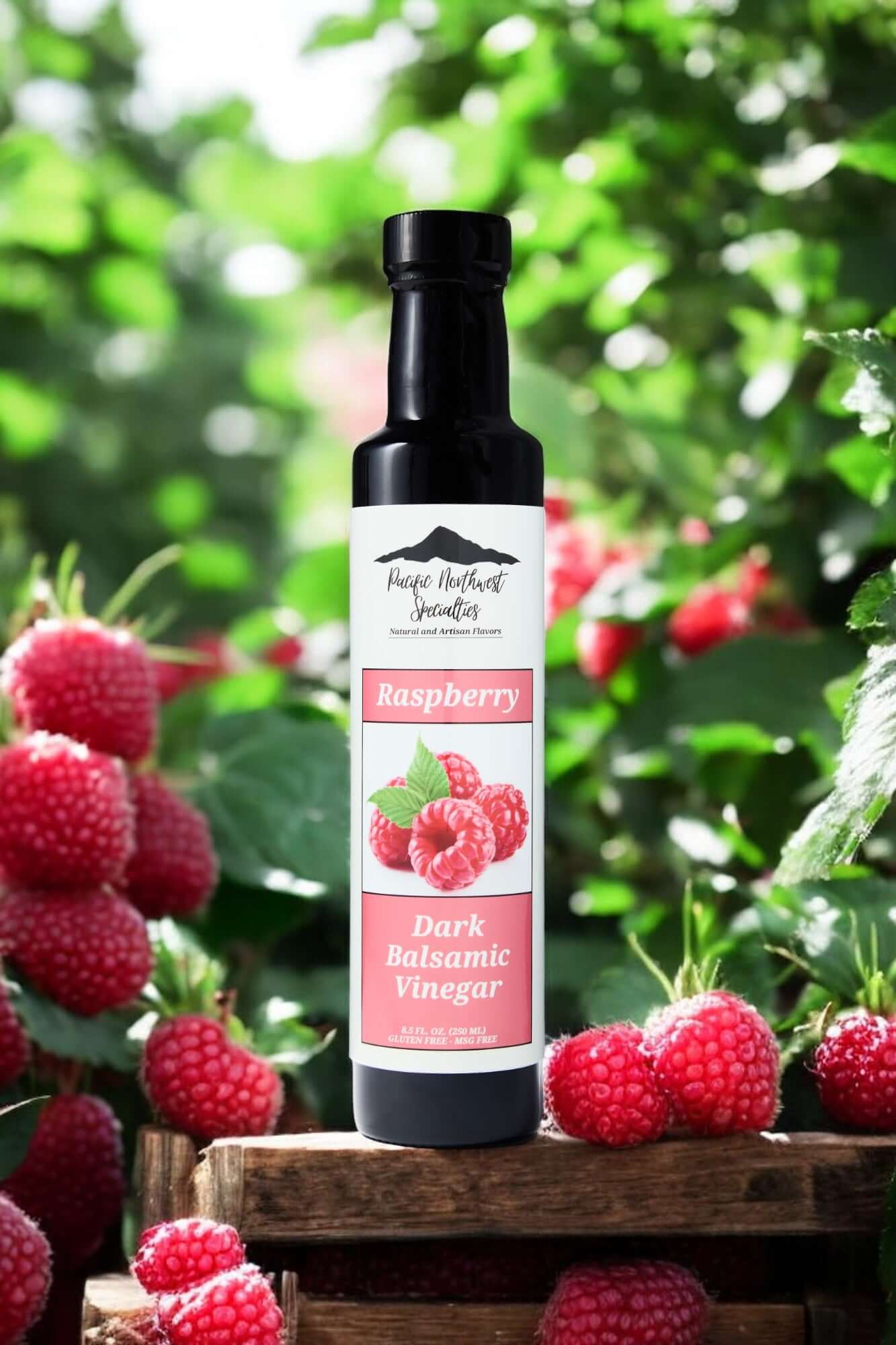 Bottle of Raspberry Dark Balsamic Vinegar surrounded by fresh raspberries in a vibrant green garden.